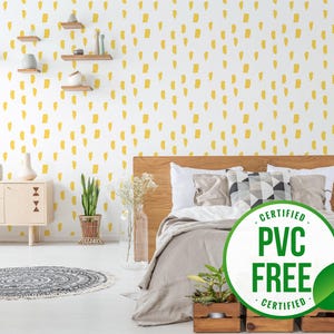 Könnte beinhalten: Eine weiße Wand mit einer gelben abstrakten Mustertapete. Ein Bett mit einer grauen Bettdecke und Kissen steht vor der Wand. Eine grüne Pflanze steht in einem Topf auf dem Boden. Ein Schild lautet "ZERTIFIZIERT PVC FREI ZERTIFIZIERT".