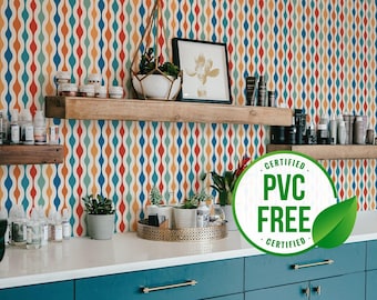 Può includere: Un armadio blu turchese con maniglie dorate davanti a una parete con un motivo geometrico colorato. La parete è decorata con piante e mensole con vari prodotti. Un cerchio verde con il testo "CERTIFIED PVC FREE CERTIFIED" è in primo piano.