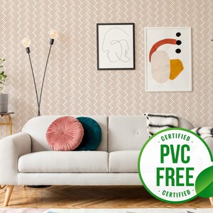 May include: A white sofa with two cushions, one pink and one teal, in a living room with a beige wallpaper featuring a geometric pattern. A black and white abstract art print and a colourful abstract art print hang on the wall. A potted plant is in the corner of the room. A sign reads "CERTIFIED PVC FREE CERTIFIED".