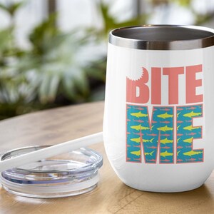K&ouml;nnte beinhalten: Ein wei&szlig;er Edelstahlbecher mit einem pinkfarbenen "Bite Me"-Motiv und einem blauen und gelben Hai-Muster. Der Becher hat einen Deckel und einen Strohhalm.