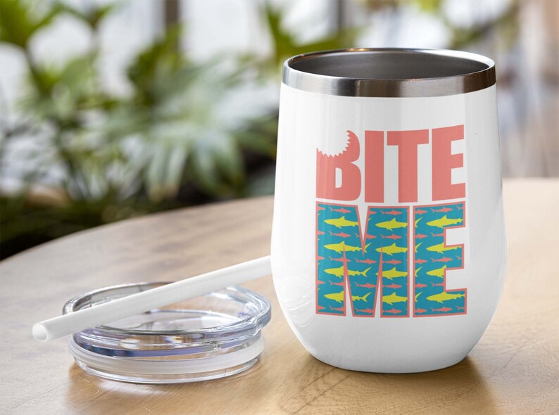 K&ouml;nnte beinhalten: Ein wei&szlig;er Edelstahlbecher mit einem pinkfarbenen "Bite Me"-Motiv und einem blauen und gelben Hai-Muster. Der Becher hat einen Deckel und einen Strohhalm.