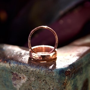 May include: Two gold wedding bands stacked on top of each other, sitting on a textured, green surface.