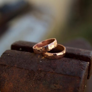 May include: Two hammered copper rings stacked on top of each other, resting on a rusty metal surface.