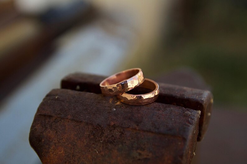 May include: Two hammered copper rings stacked on top of each other, resting on a rusty metal surface.