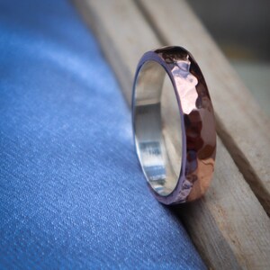 May include: A hammered copper and silver band ring. The ring has a textured, hammered finish and is a unique piece of jewelry.