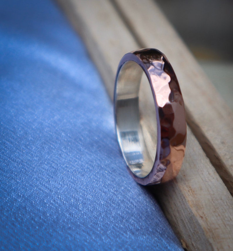 May include: A hammered copper and silver band ring. The ring has a textured, hammered finish and is a unique piece of jewelry.