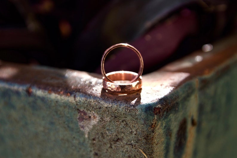 May include: Two gold wedding bands stacked on top of each other, sitting on a textured, green surface.