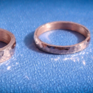 Puede incluir: Tres anillos de metal martillado. Los anillos son de un color met&aacute;lico c&aacute;lido, posiblemente dorado o bronce. Cada anillo tiene una superficie texturizada y facetada, que captura la luz. Los anillos est&aacute;n sobre un fondo azul.