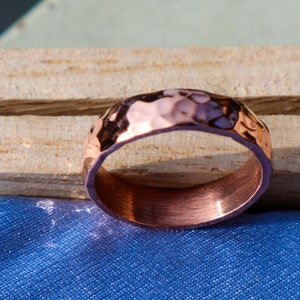 May include: A hammered copper ring with a brushed finish. The ring is a simple band with a textured surface.