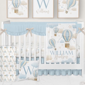 Puede incluir: Un juego de guardería con una cuna blanca, ropa de cama azul claro y arte mural a juego. El arte presenta globos aerostáticos, nubes y estrellas. También se incluye una almohada y una manta.