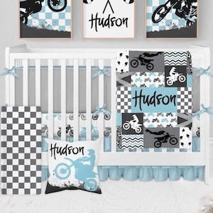 Puede incluir: Un juego de cama infantil que incluye una cuna blanca, una colcha de patchwork con gráficos de motocross y el nombre Hudson, un cojín a juego con el nombre Hudson y tres cuadros de pared con banderas a cuadros y pilotos de motocross.