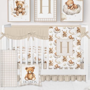 May include: A nursery set featuring a white crib with a beige bumper, sheets, and a decorative pillow. Three framed prints above the crib depict a teddy bear on a swing, a letter "H", and a teddy bear on a cloud. The set has a soft, neutral color palette.
