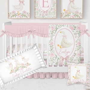 May include: A nursery set with a white crib, bedding, and wall art featuring a goose design with pink bows and floral accents. The set includes a crib bumper, blanket, pillow, and framed prints. The crib is decorated in shades of pink and white.