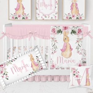 May include: A nursery set with a pink and white cot, bedding, and wall art. The set includes a cot, a cot bumper, a blanket, a pillow, and three framed prints featuring a bunny and floral designs. The name "Maria" is featured on the pillow and blanket.