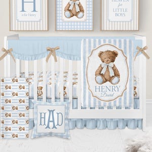 May include: A white crib set featuring a light blue and white striped pattern with teddy bear illustrations. The set includes a blanket with the name Henry David, a pillow with the monogram HAD, and three framed wall prints with teddy bear art.