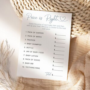 May include: A white card with the text "Price is Right" in blue script with a heart symbol. The card has a list of baby items with blank spaces to write in the price of each item. The card is on a light brown woven surface.