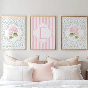 May include: Three framed wall art prints with gold frames. The two outer prints feature a pink hydrangea flower centered on a blue and white trellis pattern. The center print displays a large pink letter E on a pink and white vertical striped background.