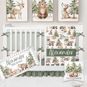 May include: A nursery set featuring a white crib with green accents and woodland-themed bedding. The set includes framed art prints of a deer, bear, and fox. A pillow and a decorative name banner are also included, all with a forest animal theme.