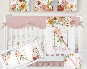 Könnte beinhalten: Ein Kinderzimmer-Set mit einem weißen Kinderbett, einem rosa Bettumrandung und floraler Bettwäsche. Das Set enthält eine Decke, Kissen und gerahmte Kunstdrucke, alle mit Aquarell-Blumenmustern verziert. Die Decke ist mit einem Namen personalisiert.