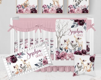 May include: A pink and white crib bedding set with a woodland theme. The bedding features a fox, deer, and raccoon with floral accents. The crib skirt is pink with ruffles. The blanket is white with a floral design and the text "Sophia Grace".