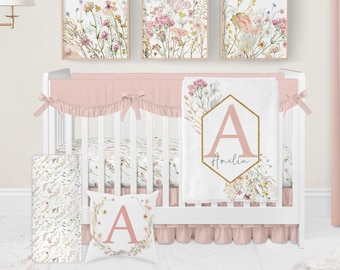 Könnte beinhalten: Ein weißes Babybett mit einem rosa und floralen Babybettwäsche-Set. Die Bettwäsche umfasst ein Spannbettlaken, einen Stoßfänger, eine Decke und ein Kissen. Die Decke hat ein goldenes Sechseck mit dem Buchstaben A und dem Namen Amelia. Das Babybett steht in einem Kinderzimmer mit einem rosa Vorhang und drei floralen Drucken an der Wand.