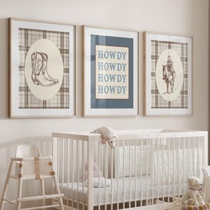 May include: A nursery scene with three framed prints featuring cowboy-themed illustrations and the word "HOWDY." A white crib, high chair, and baskets filled with stuffed animals complete the decor. The color palette is neutral with beige, white, and brown tones.