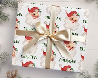 May include: White wrapping paper with a repeating pattern of Santa Claus faces and the name "Christian". A gold ribbon is tied around the paper.