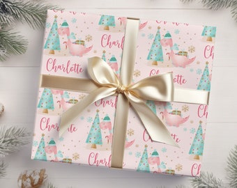 May include: Pink wrapping paper with a repeating pattern of green Christmas trees and pink dinosaurs wearing Santa hats. The paper is decorated with gold glitter and snowflakes. The name "Charlotte" is repeated throughout the paper.