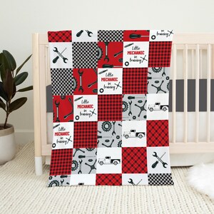 May include: Red and black checkered baby blanket with a patchwork design featuring tools, gears, and trucks. The blanket has the text "Little Mechanic in Training" repeated throughout.