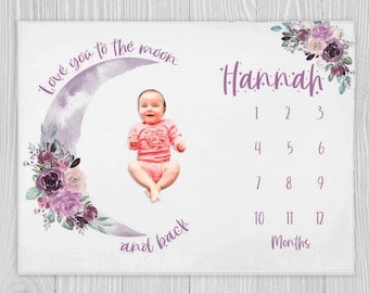 May include: A white baby milestone blanket with a purple watercolor crescent moon and floral design. The text "Love you to the moon and back" is written on the blanket. The text "Hannah" is written in purple with a number chart for each month of the year. A baby girl is sitting inside the crescent moon.