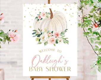 May include: White pumpkin with pink and white flowers and greenery on a white background with gold glitter. The text "Welcome to Oakleigh's Baby Shower" is below the pumpkin.