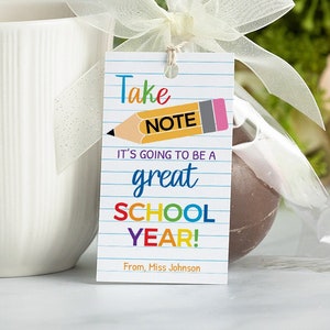 May include: A white mug with a rainbow pencil and the text "Take Note It's going to be a great school year! From Miss Johnson" on a tag attached to a chocolate-covered treat.