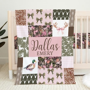 Puede incluir: Una colcha de bebé rosa y verde con un diseño de patchwork. La colcha presenta una variedad de patrones, incluyendo camuflaje, lazos y cuernos de ciervo. La colcha está personalizada con el nombre "Dallas Emery".