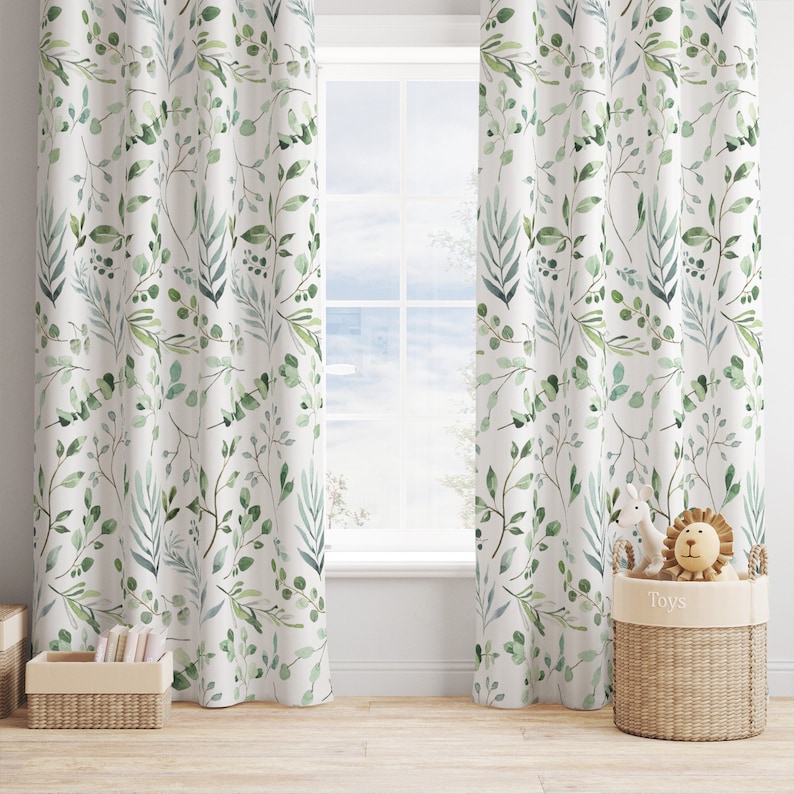 May include: White curtains with a watercolor-style botanical print featuring green leaves and branches. The curtains hang in front of a window, with a glimpse of the outdoors visible. A woven basket with toys sits nearby.