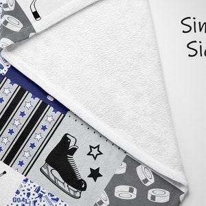May include: A single-sided fleece blanket with a patchwork design featuring hockey-themed patterns. The patterns include hockey sticks, pucks, skates, and the word "GOAL!" in a blue and white color scheme.
