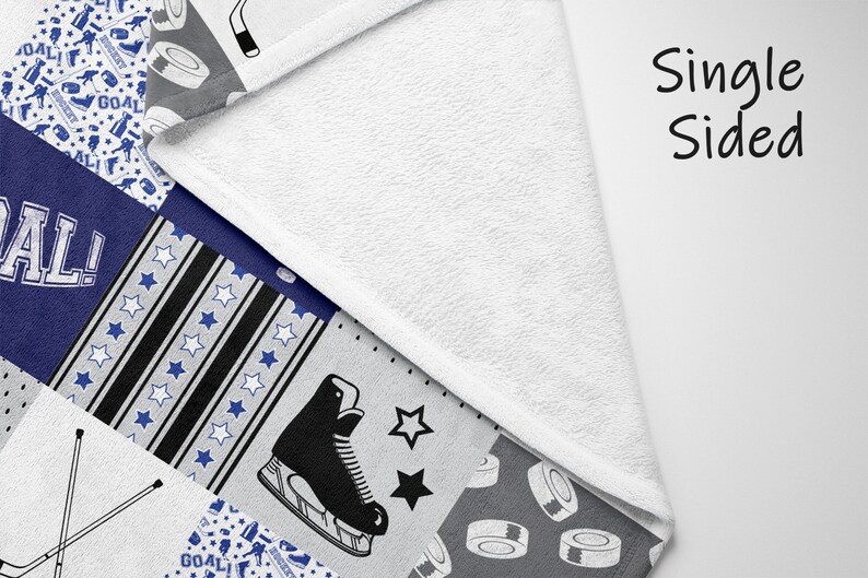 May include: A single-sided fleece blanket with a patchwork design featuring hockey-themed patterns. The patterns include hockey sticks, pucks, skates, and the word "GOAL!" in a blue and white color scheme.