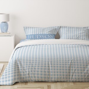 May include: A blue and white gingham duvet cover with a white pillow with the word "HUDSON" printed on it.