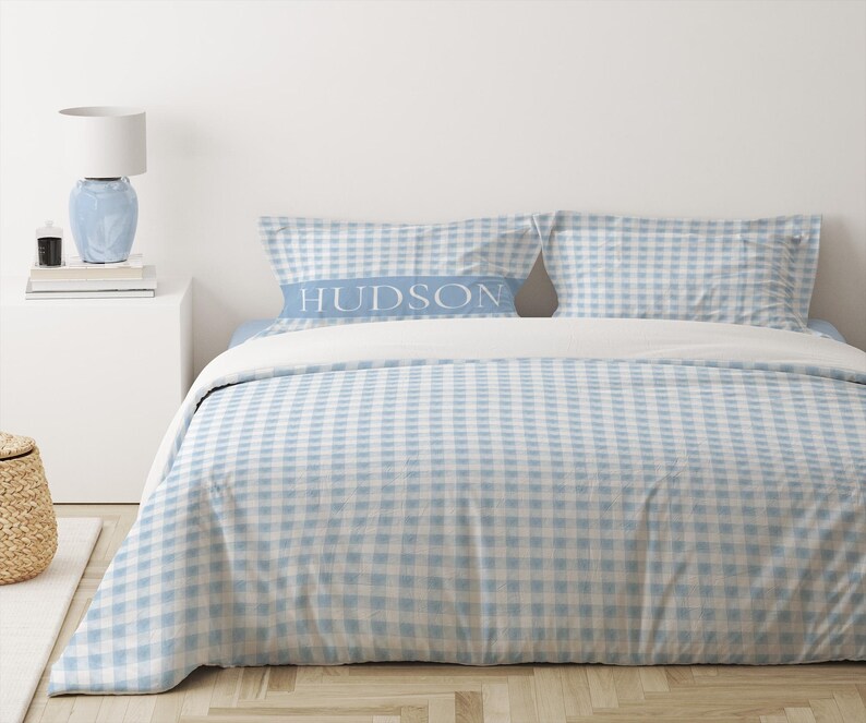 May include: A blue and white gingham duvet cover with a white pillow with the word "HUDSON" printed on it.