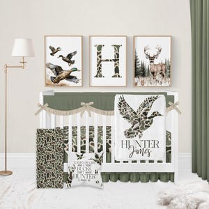 May include: A nursery set with a woodland theme. The set includes a crib, bedding, and wall art. The bedding features a camouflage pattern. The wall art includes a framed letter "H", a deer, and flying ducks. A pillow reads "CAMO DUCKS AND POINT BUCKS, THAT'S WHAT HUNTER IS MADE OF."