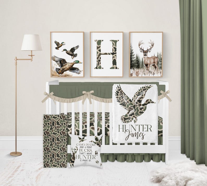 May include: A nursery set with a woodland theme. The set includes a crib, bedding, and wall art. The bedding features a camouflage pattern. The wall art includes a framed letter "H", a deer, and flying ducks. A pillow reads "CAMO DUCKS AND POINT BUCKS, THAT'S WHAT HUNTER IS MADE OF."