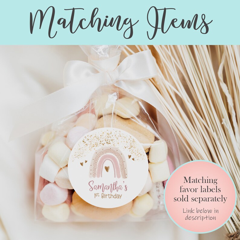 May include: A clear cellophane bag filled with pastel-colored marshmallows and cookies tied with a white ribbon. A round sticker with a pink and gold rainbow design and the text "Samantha's 1st Birthday" is attached to the bag.