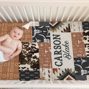 Op de afbeelding: Een bruin, zwart en wit gepatroneerd babybedlaken met een gepersonaliseerde naam, "CARSON BLAKE", in een vintage lettertype.