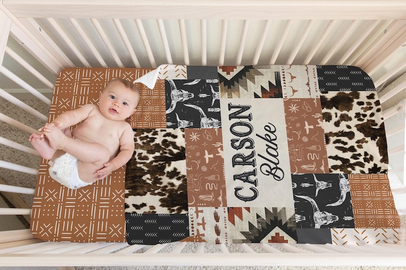 Op de afbeelding: Een bruin, zwart en wit gepatroneerd babybedlaken met een gepersonaliseerde naam, "CARSON BLAKE", in een vintage lettertype.
