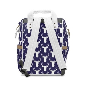 May include: A navy blue backpack with white deer silhouettes printed all over. The backpack has white straps and a brown leather accent on the side.