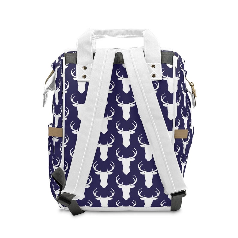 May include: A navy blue backpack with white deer silhouettes printed all over. The backpack has white straps and a brown leather accent on the side.