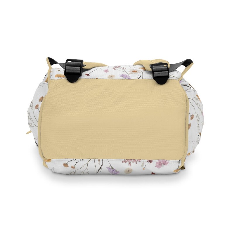 May include: A beige backpack with adjustable straps and a white floral print. The backpack has a large compartment and a smaller pocket on the front.