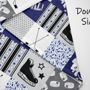 May include: A double-sided fleece blanket with a hockey theme. The blanket features a patchwork design with various hockey-related images, including hockey sticks, skates, pucks, and the word "GOAL!" in a blue and white color scheme.