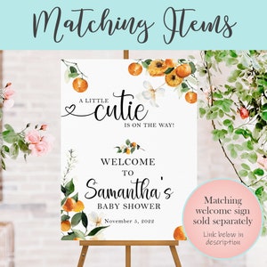 May include: A white welcome sign with orange blossoms and greenery. The sign reads "A little cutie is on the way! Welcome to Samantha's Baby Shower November 5, 2022".