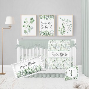 May include: A nursery set with a white crib, sage green bedding, and three framed botanical prints. The prints feature watercolor greenery and the words "You are so loved." A decorative pillow and name sign are also included.