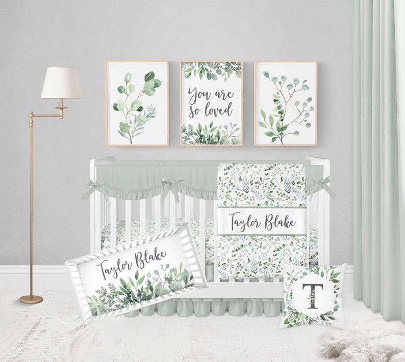 May include: A nursery set with a white crib, sage green bedding, and three framed botanical prints. The prints feature watercolor greenery and the words "You are so loved." A decorative pillow and name sign are also included.